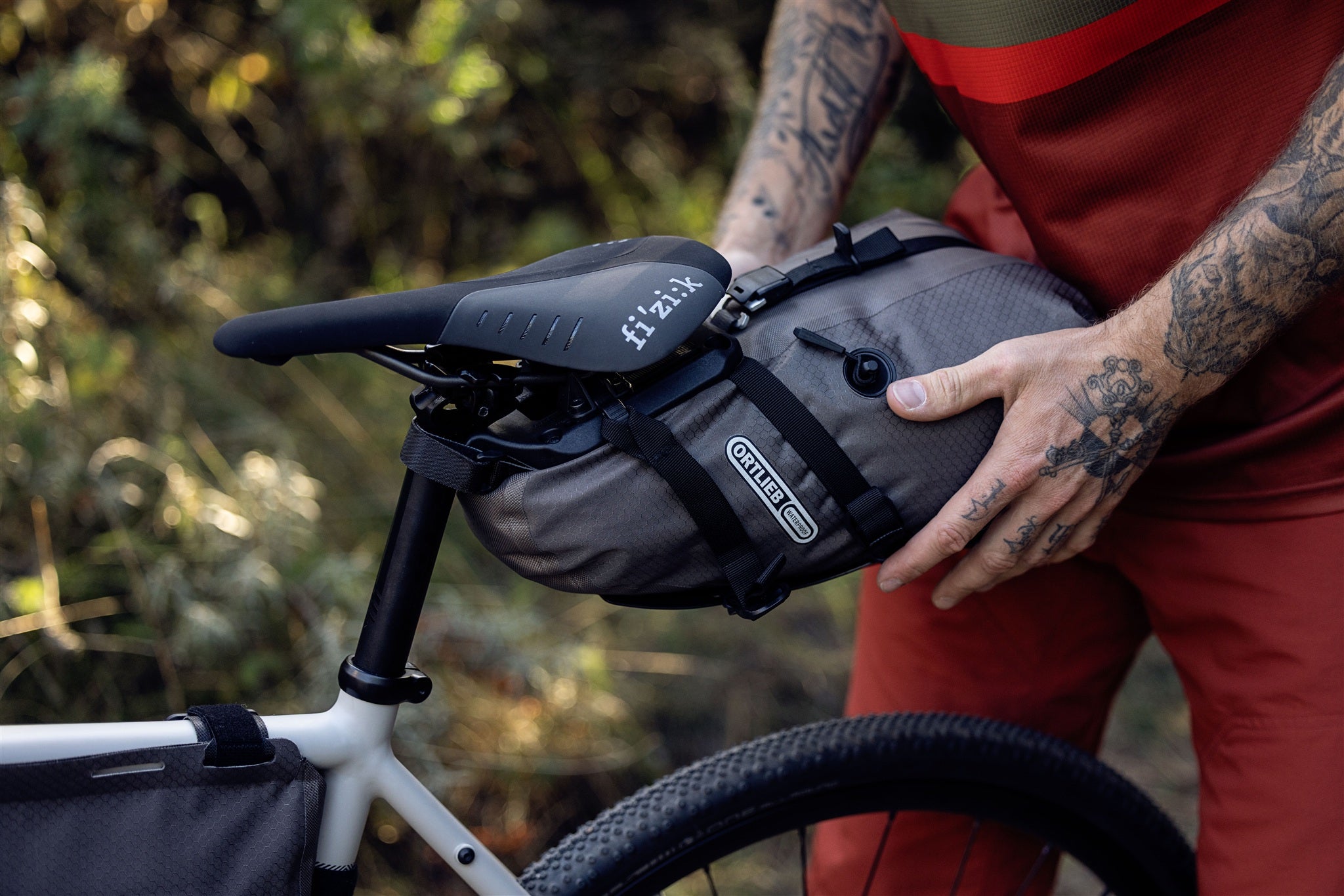 Cyclist attaching ORTLIEB Seat-Pack QR in dark-sand to bike saddle in forest